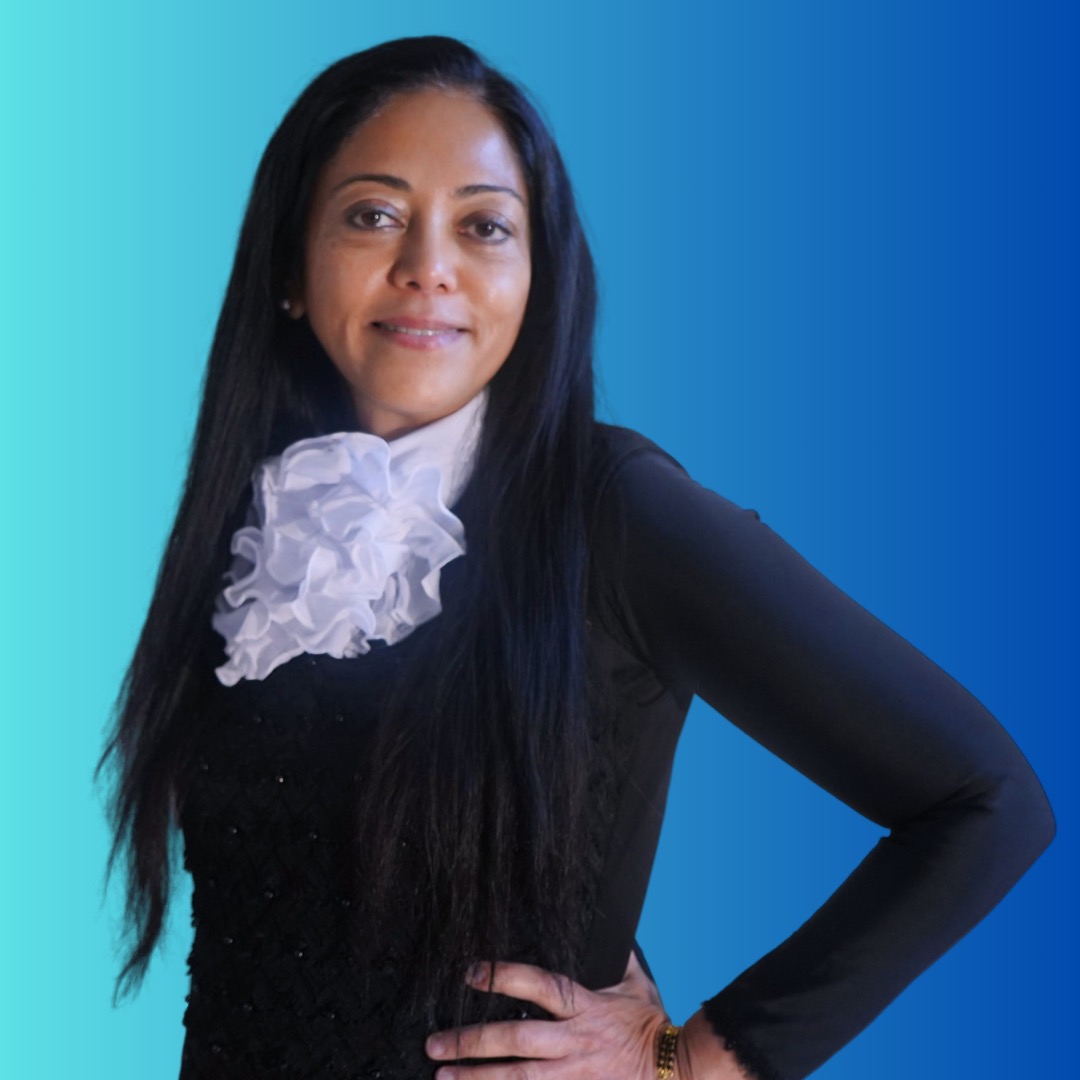 Renuka J. Lakhani in a black beaded jacket with a white jabot, against a blue background